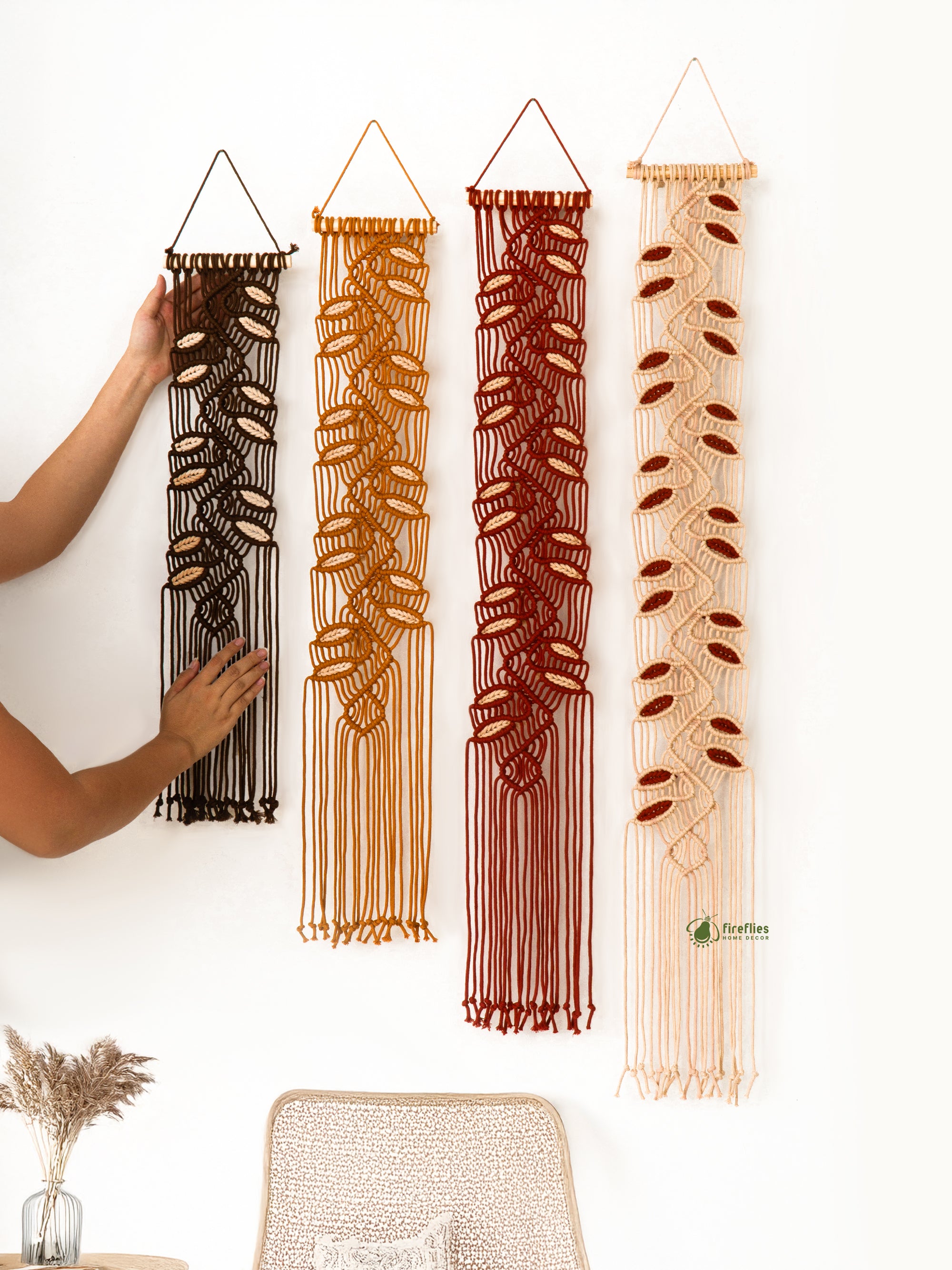Four macrame wall hangings in different colors hanging on a white wall.