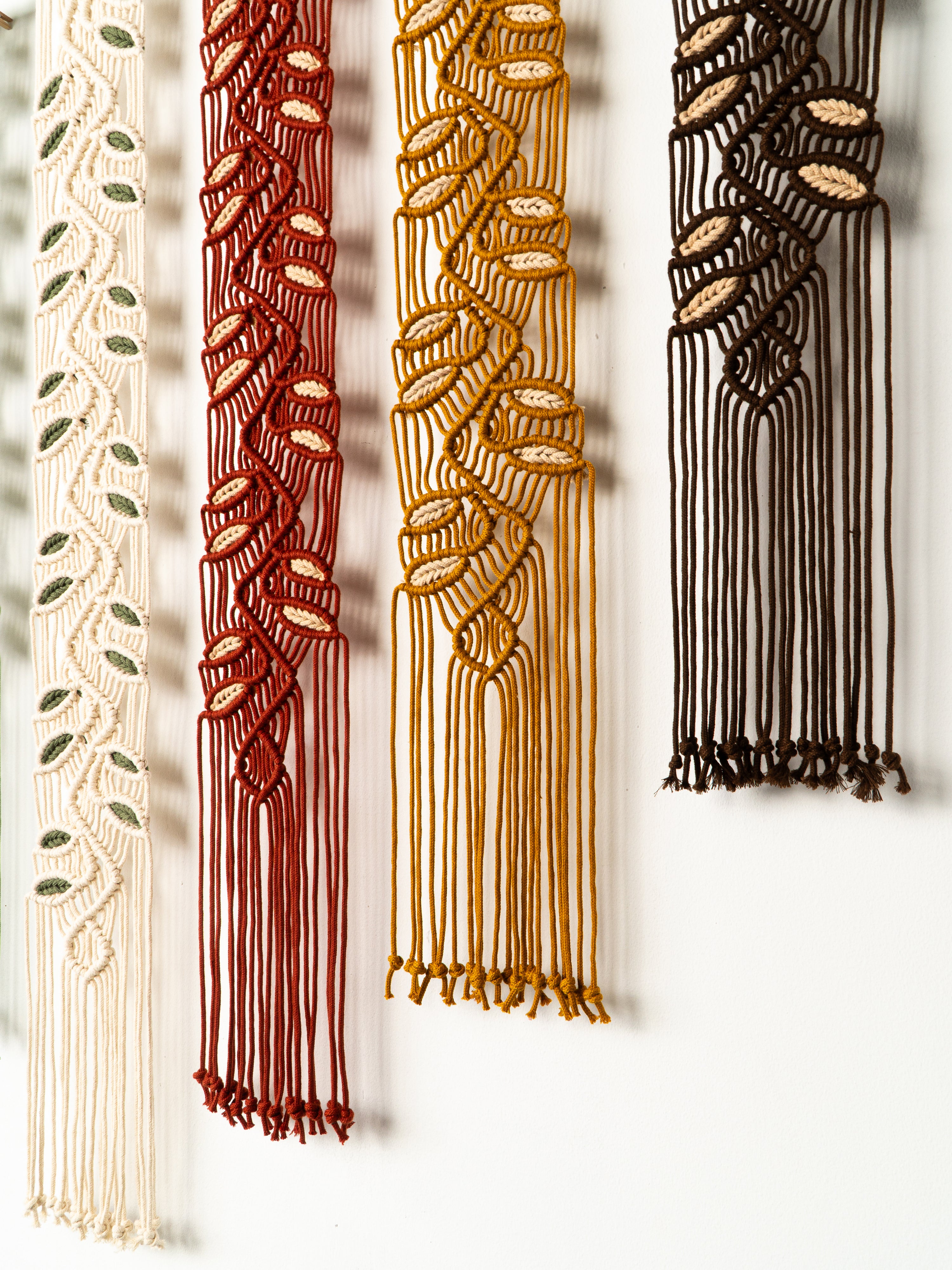 Four macrame wall hangings in different colors on a white background