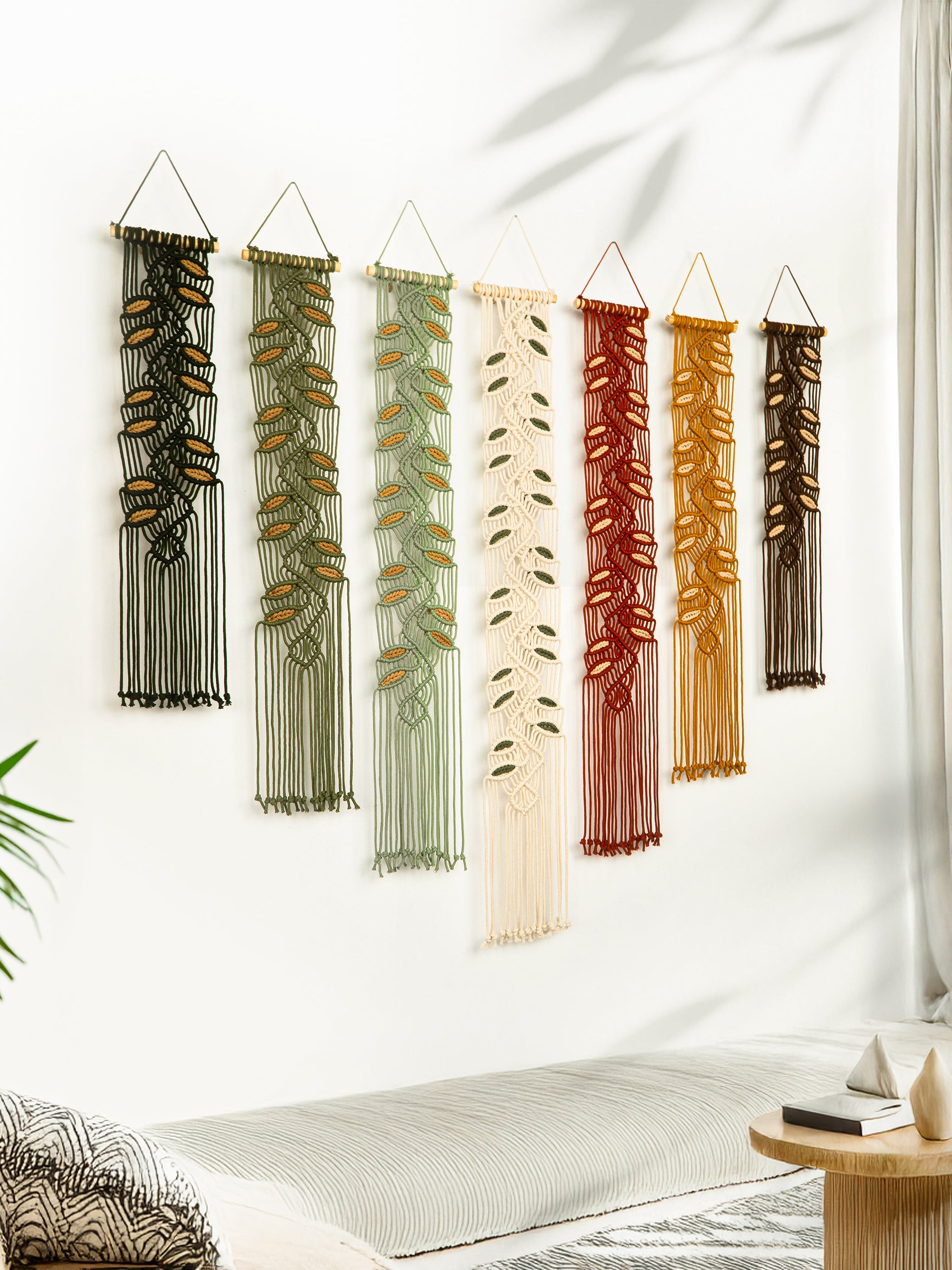 Set of six colorful wall hangings with leaf patterns on a white wall.
