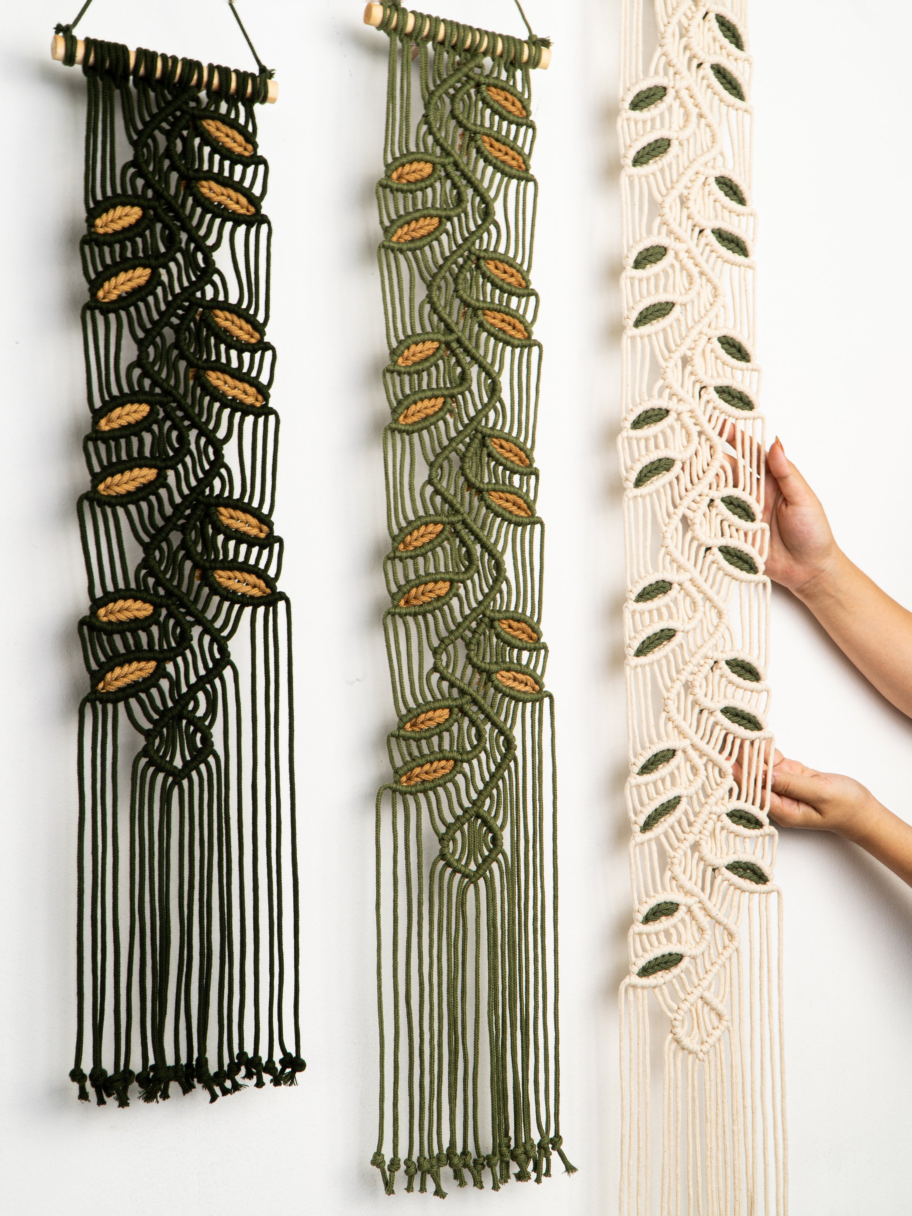 Three macrame wall hangings in black, green, and beige on a white background.