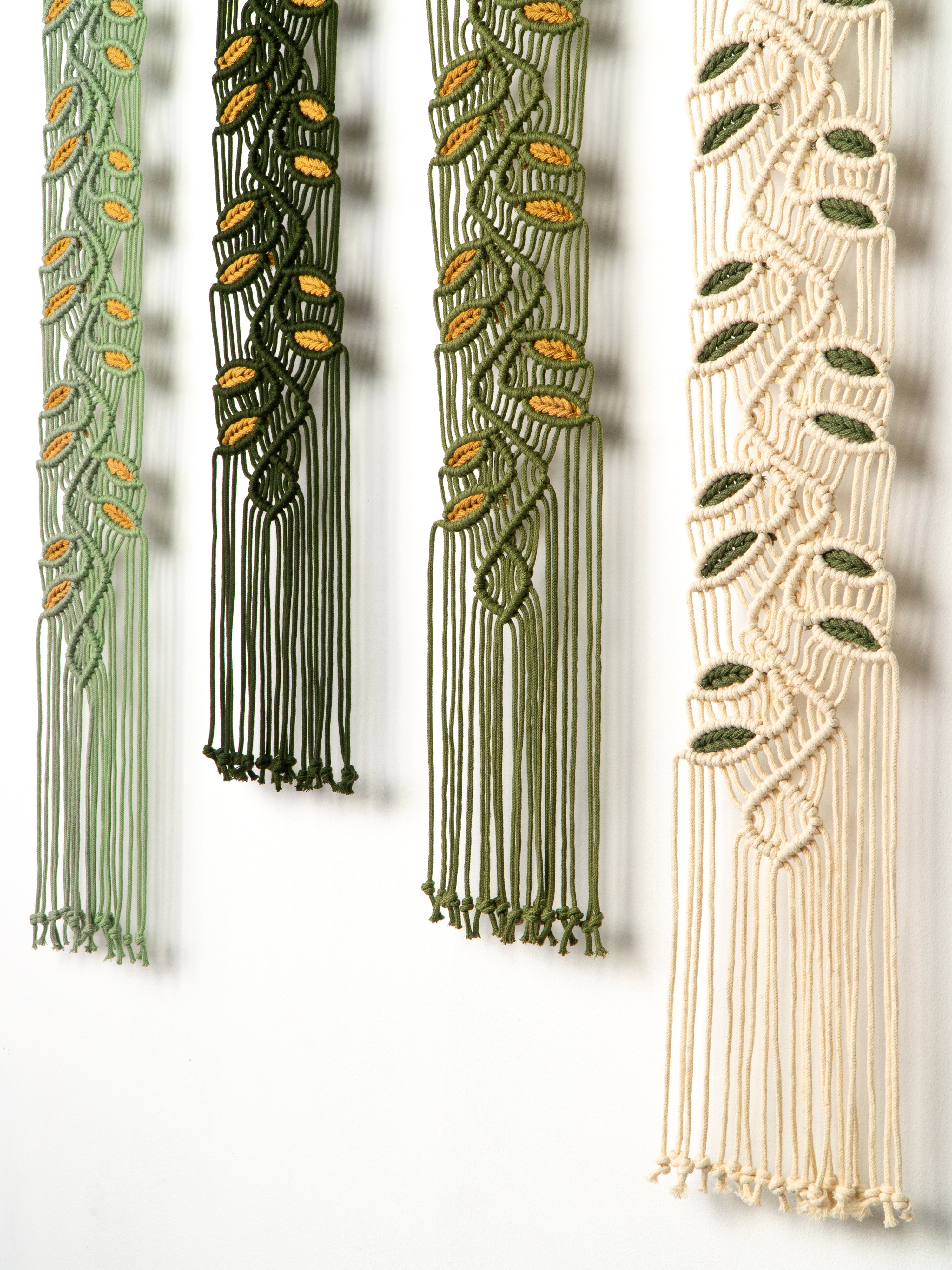 Four macrame plant hangers in green and beige with leaf patterns on a white background.