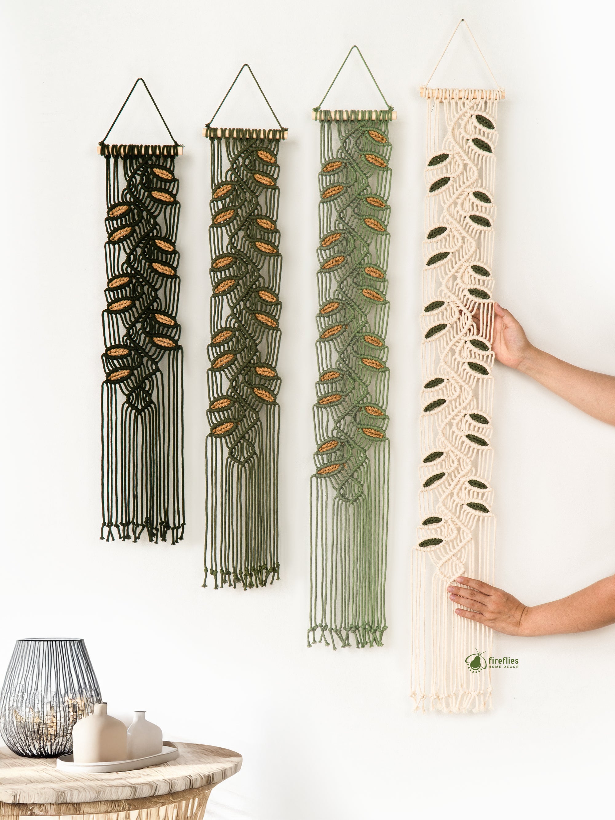 Set of four macrame wall hangings in different colors being arranged by a person.