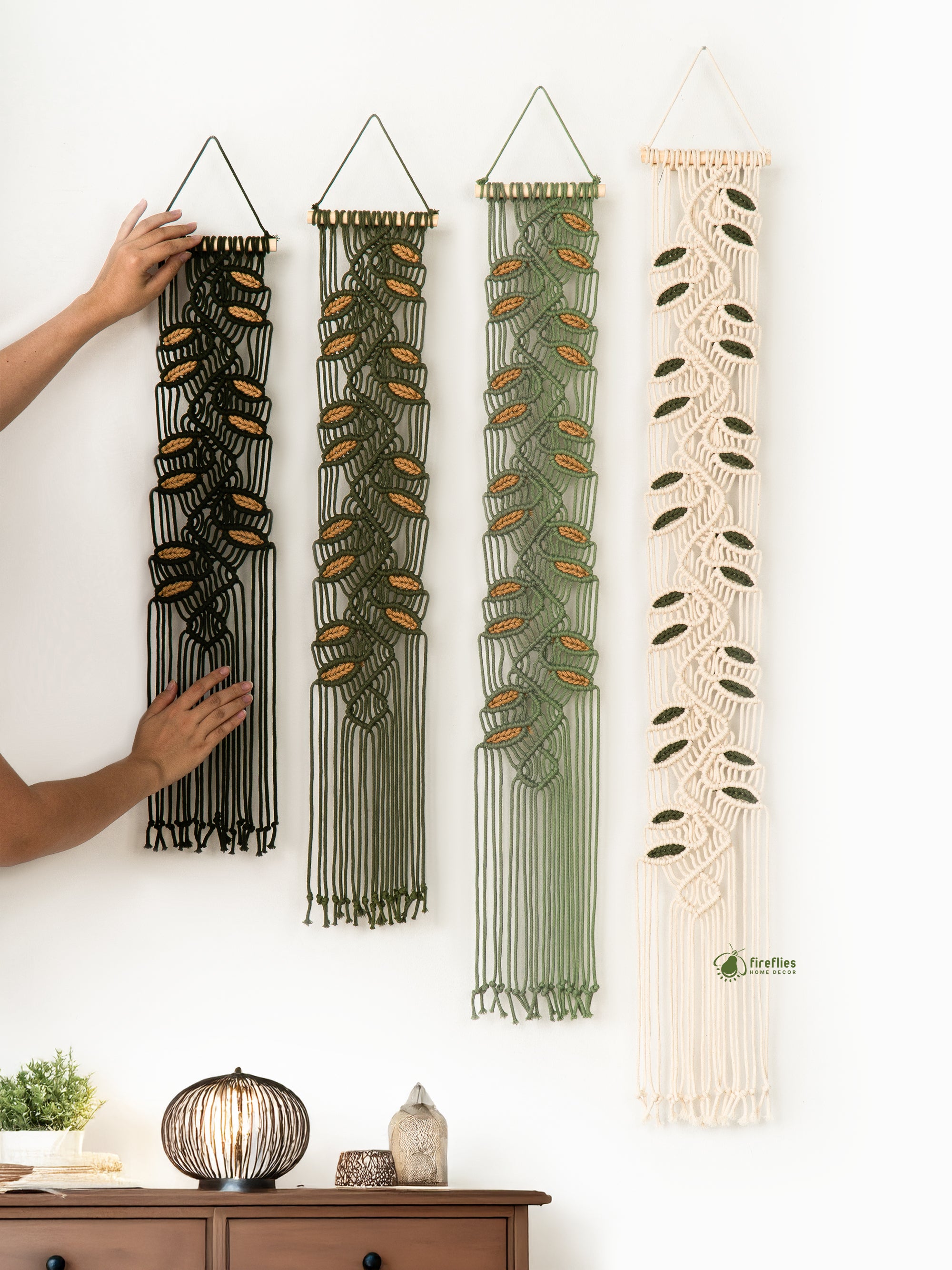 Four macrame wall hangings in different colors hanging on a white wall.