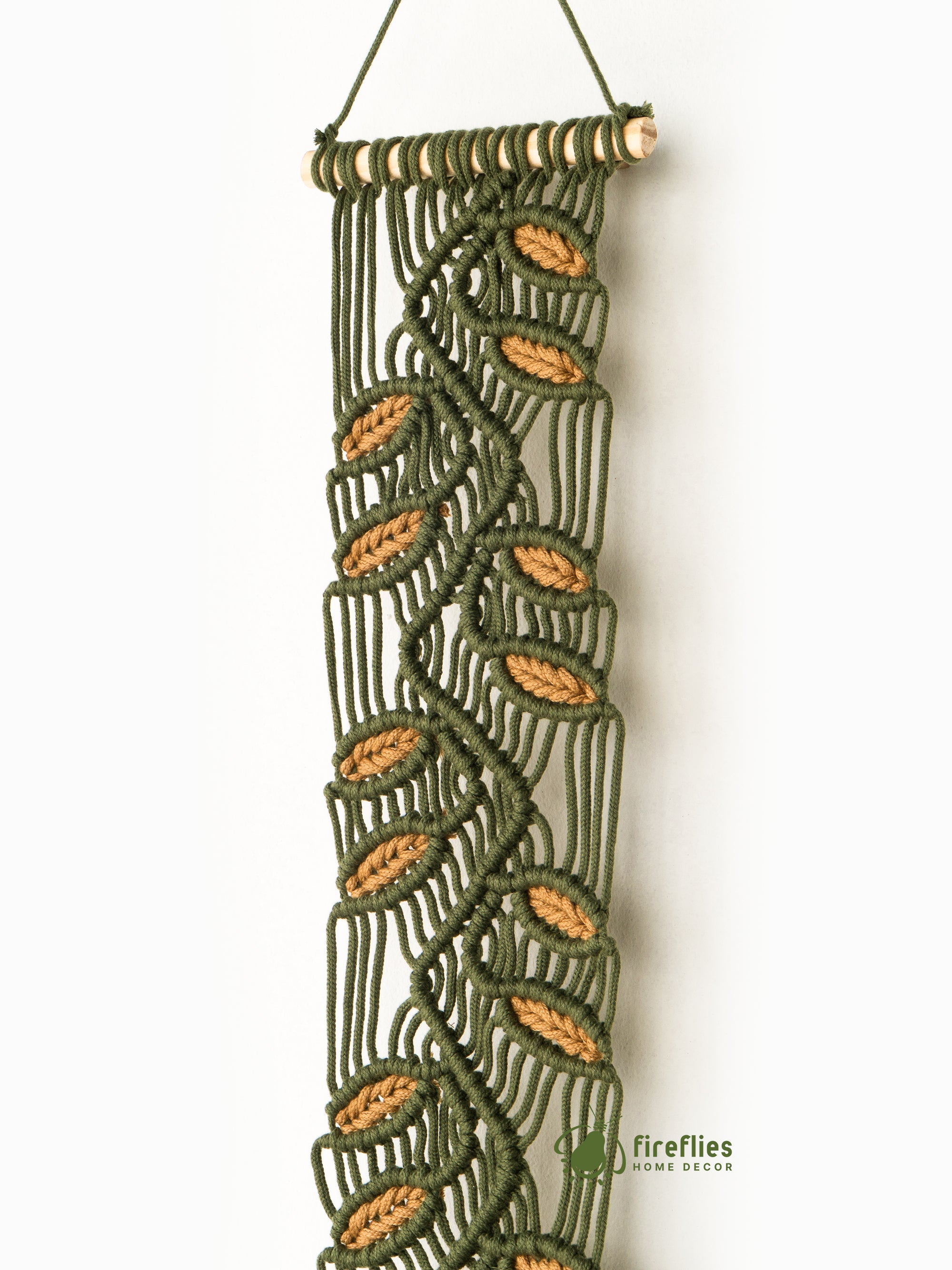 Beige woven wall hanging with fringe on a white wall above a bed.