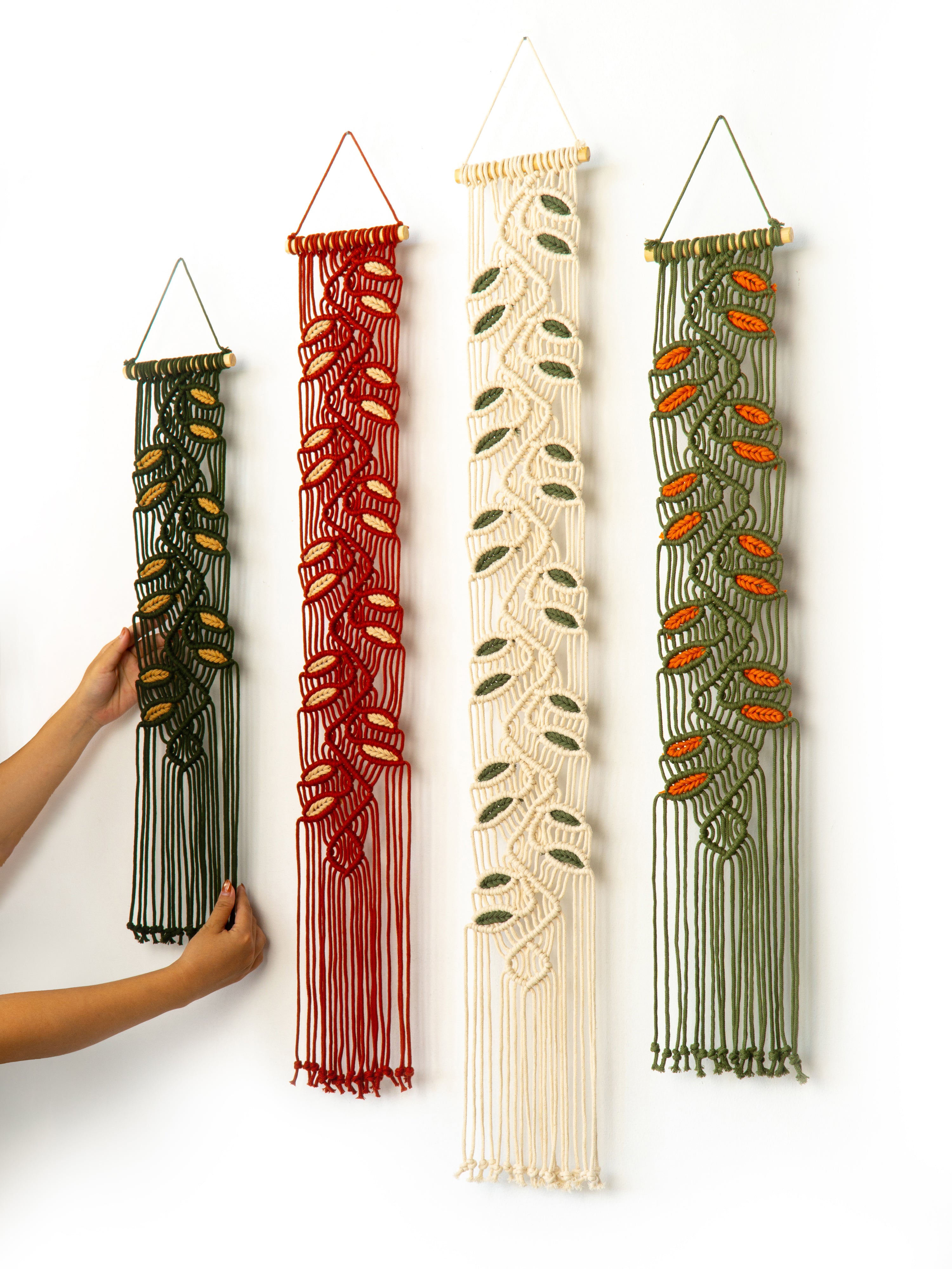 Four macrame wall hangings in different colors on a white background