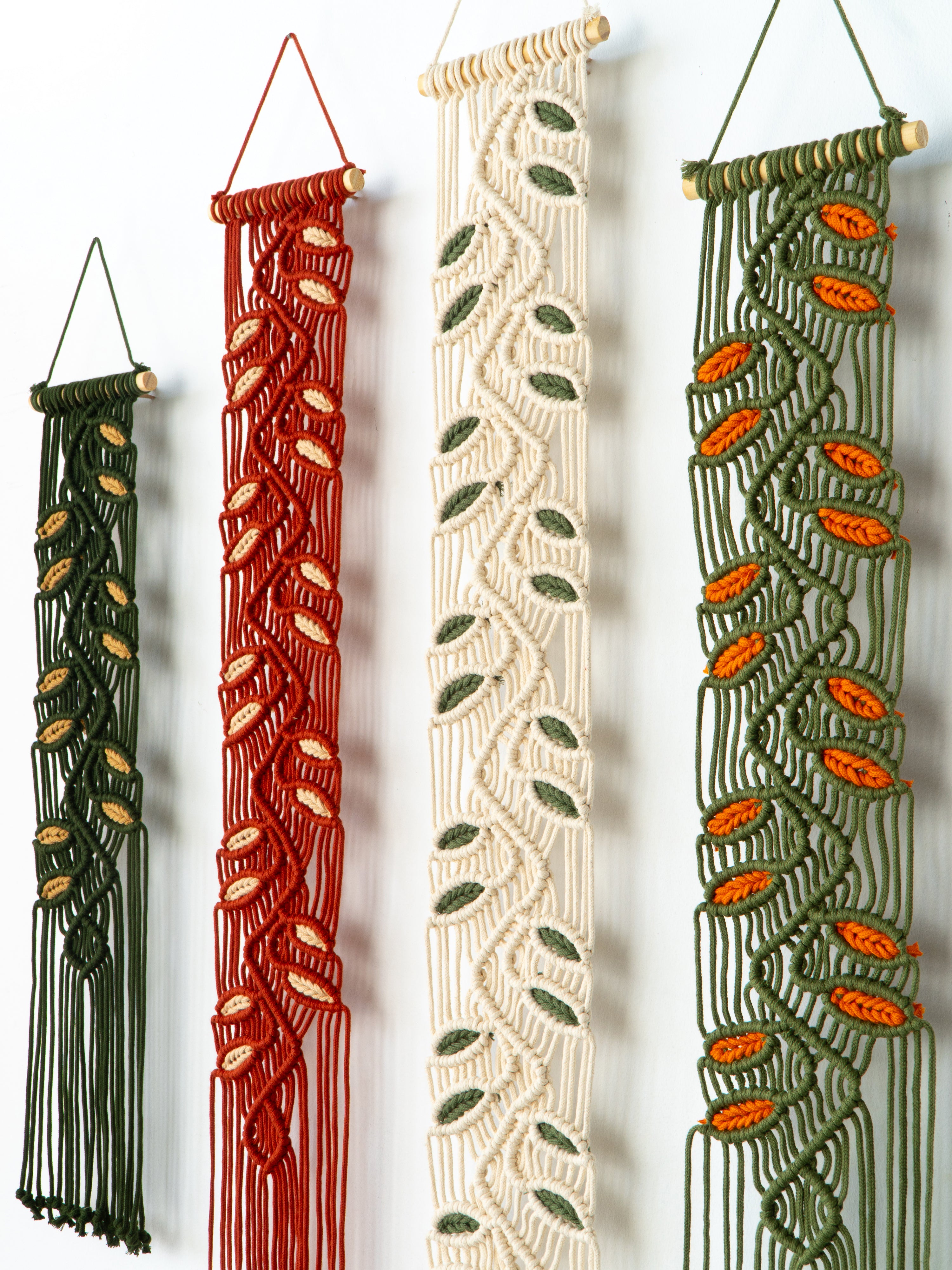 Four macrame wall hangings in different colors hanging against a white background.