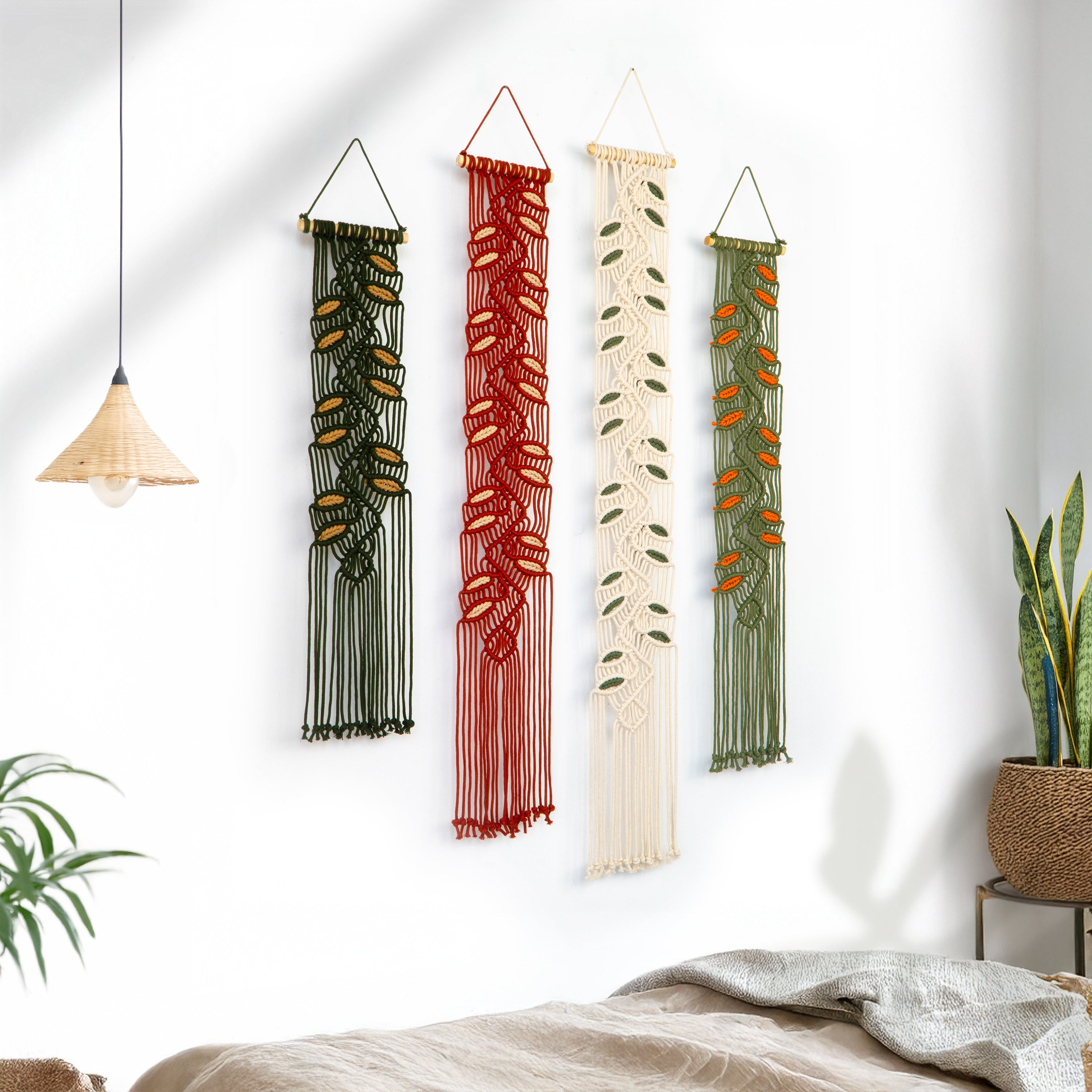 Four macrame wall hangings in different colors hanging on a white wall.