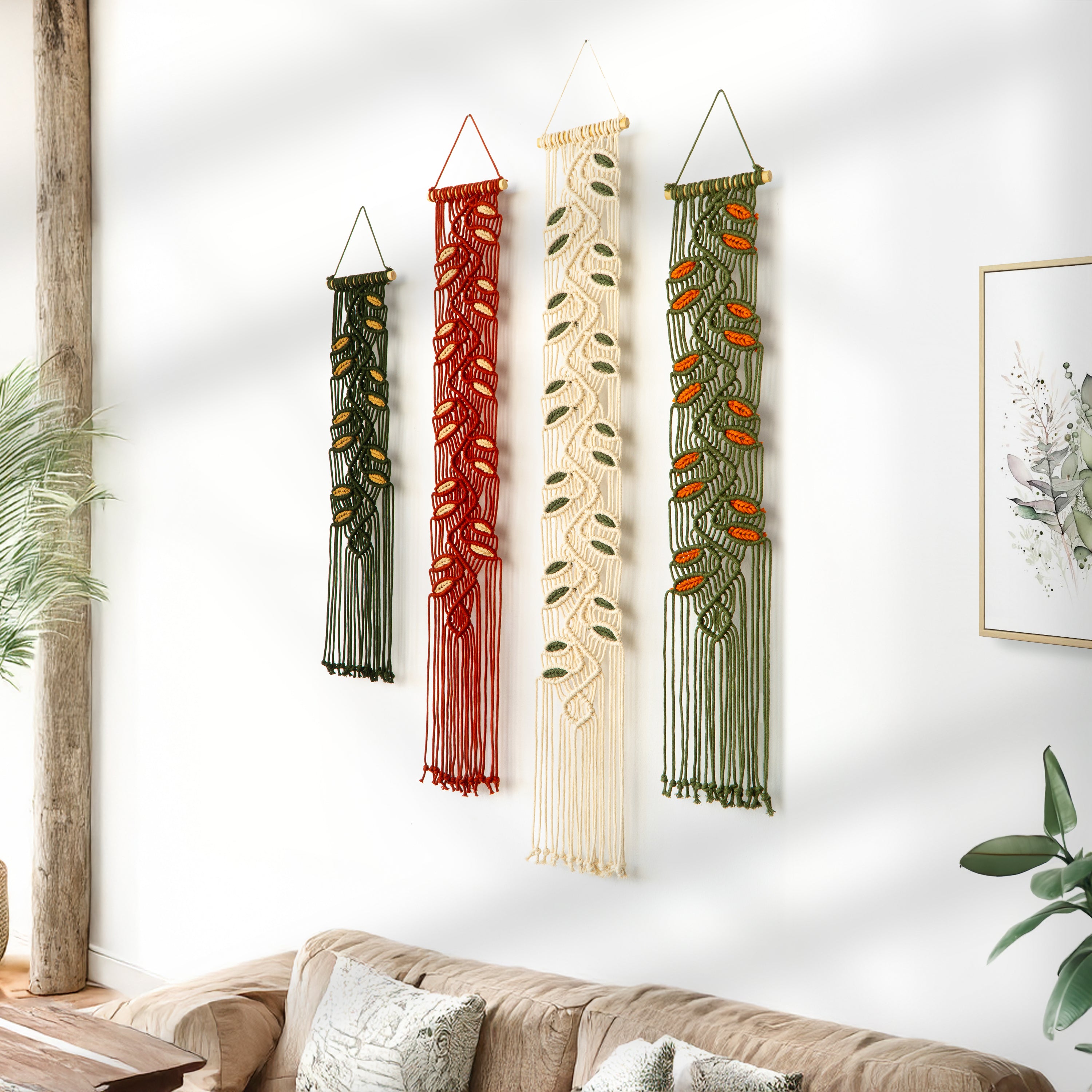 Four macrame wall hangings in various colors hanging on a white wall above a sofa.