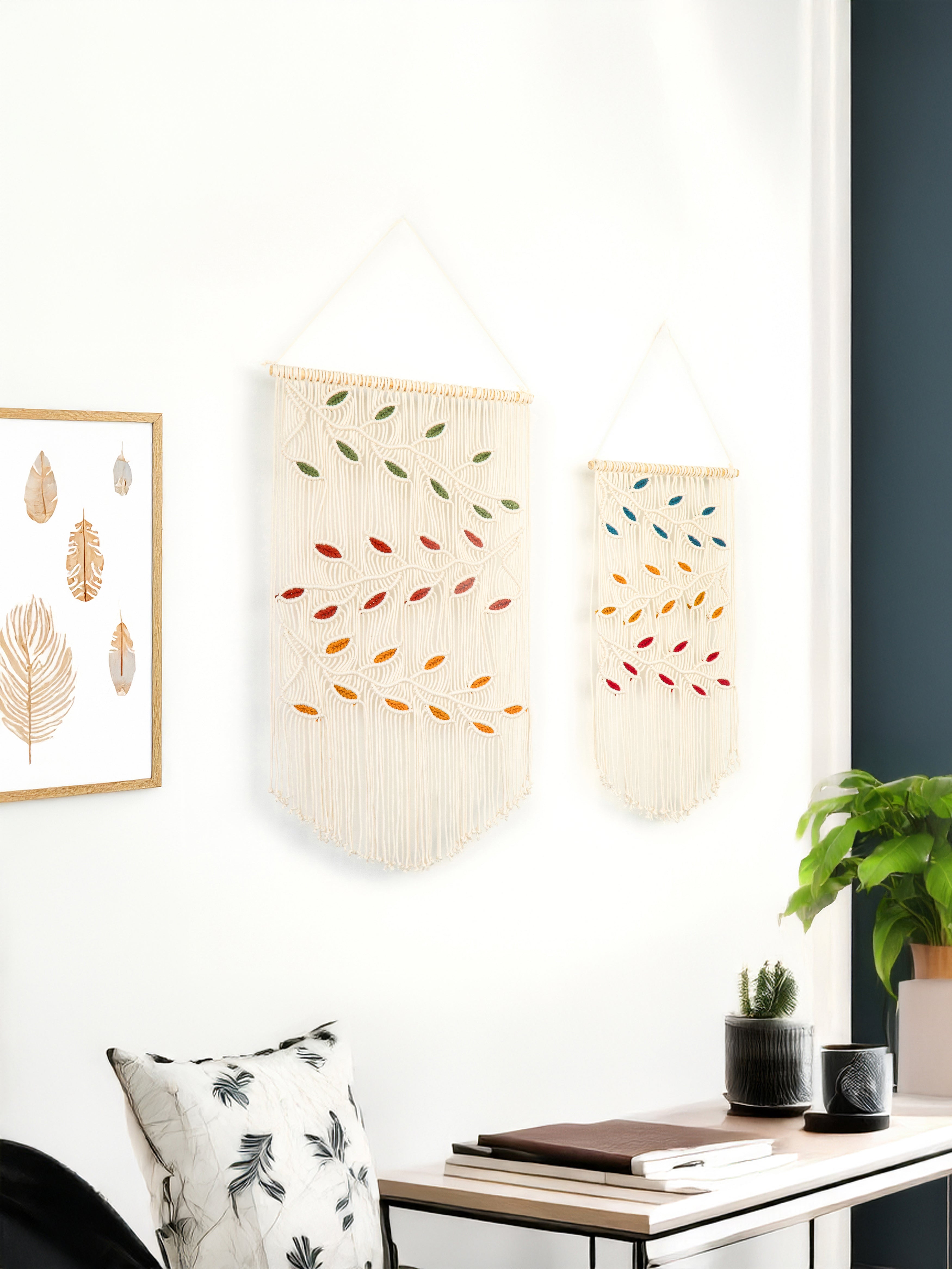 Decorative wall hangings with leaf patterns on a white wall in a room with a desk and plant.