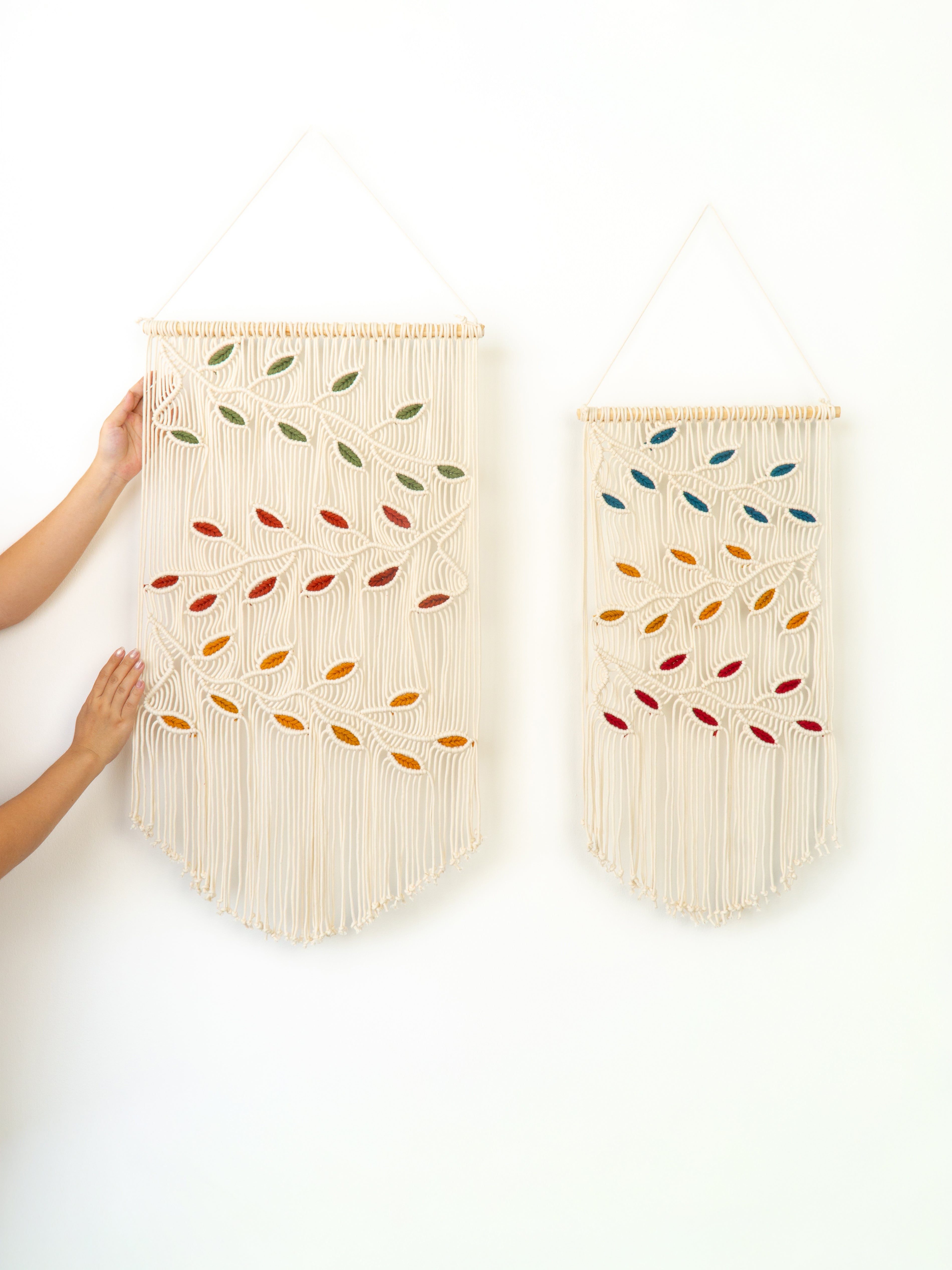 Two wall-mounted woven wall hangings with colorful leaf patterns on a white background.