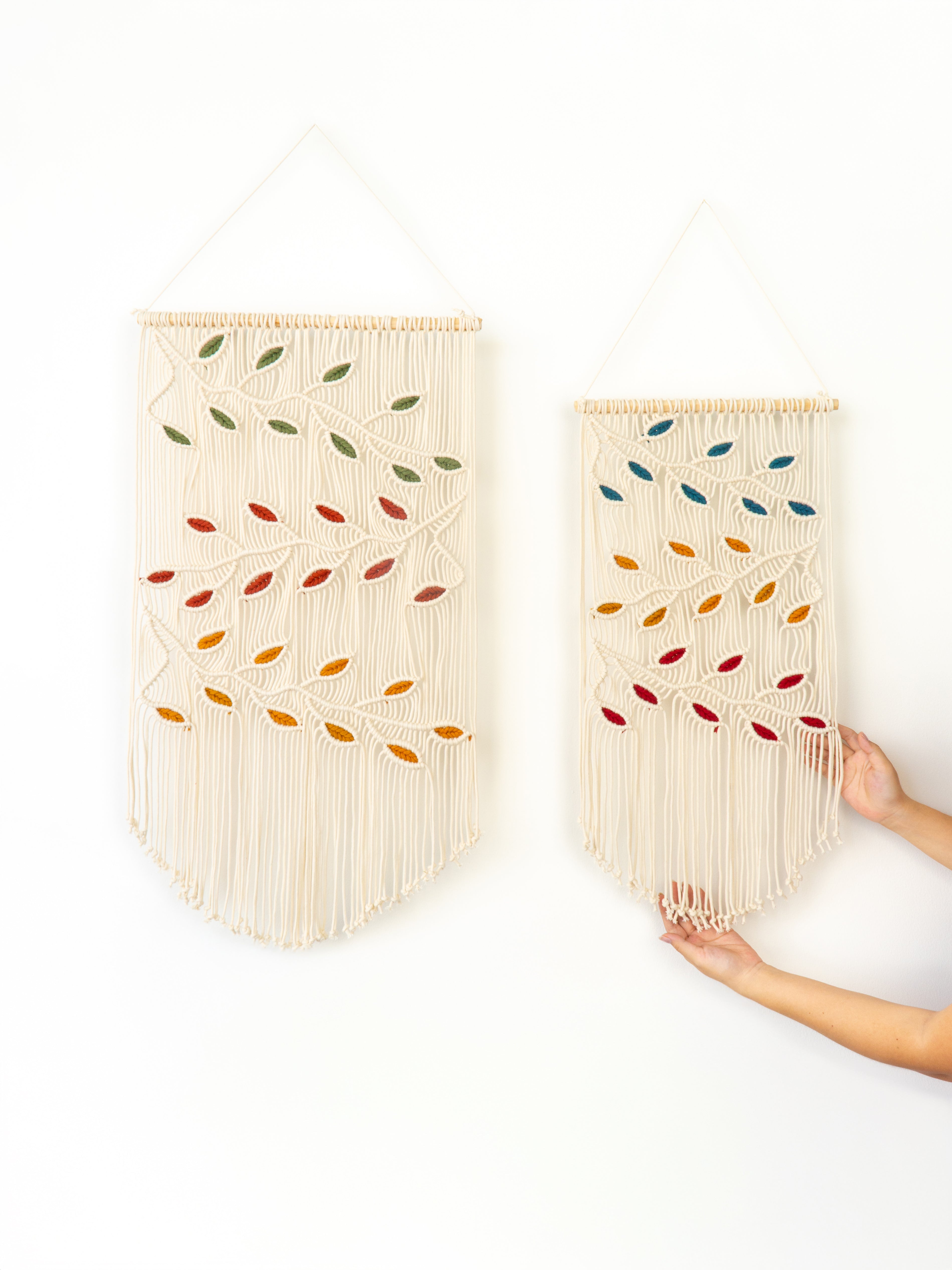 Two woven wall hangings with colorful leaf patterns on a white background