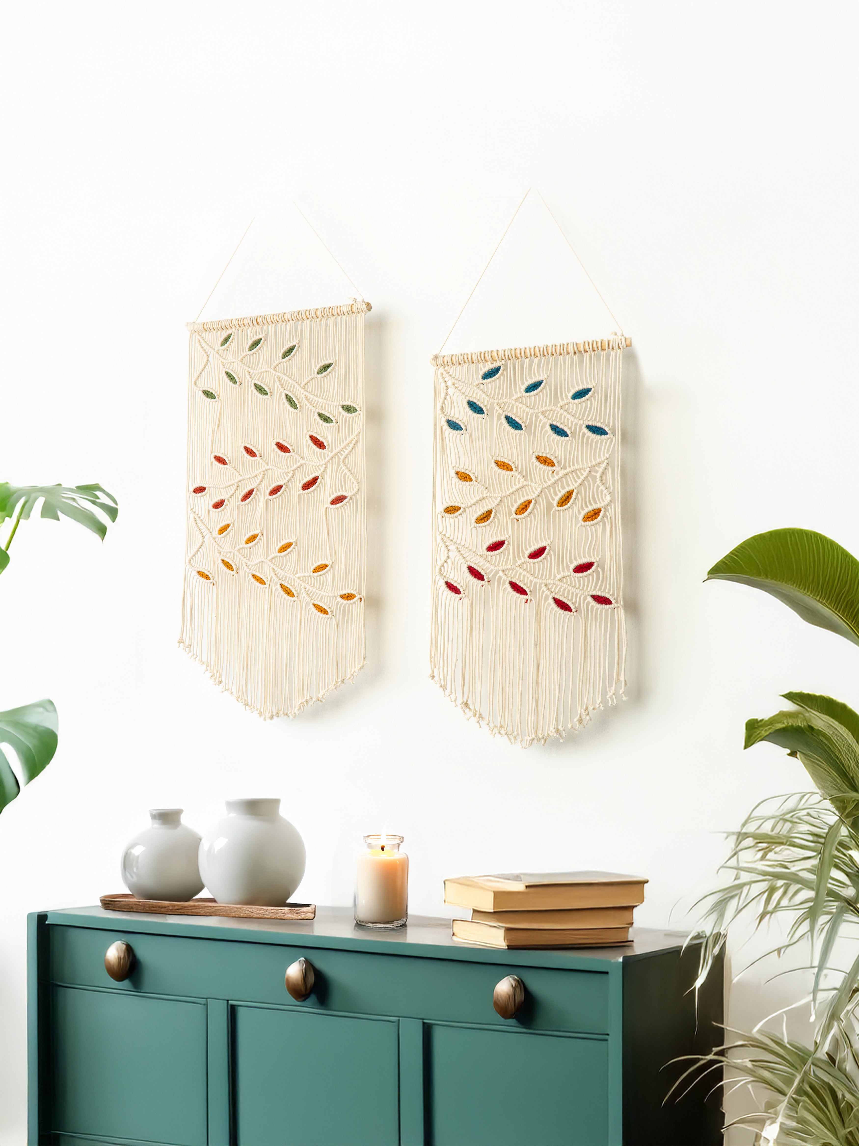 Two decorative wall hangings with colorful leaf patterns on a white wall above a green cabinet.