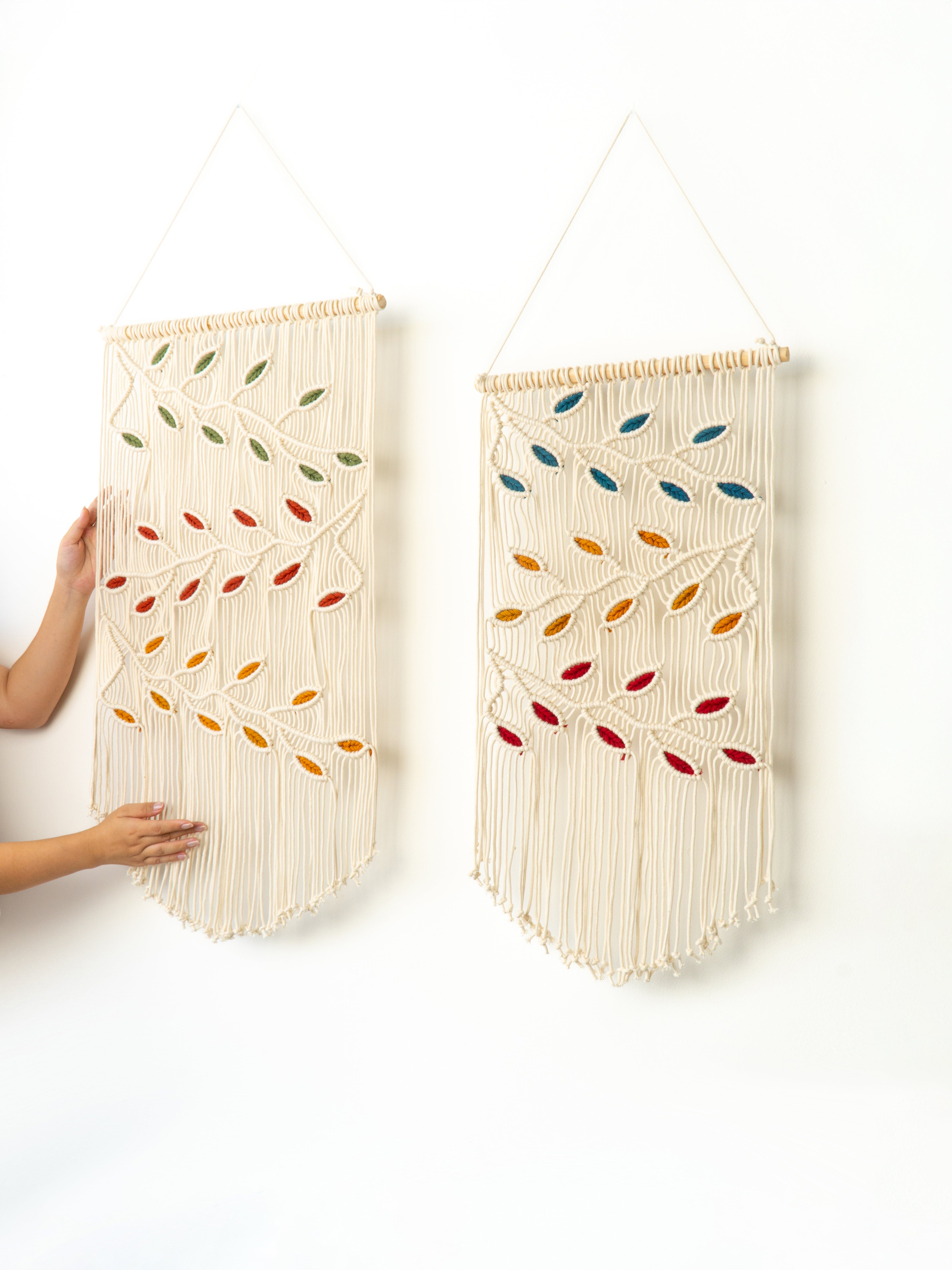 Two wall hangings with colorful leaf patterns on a white background