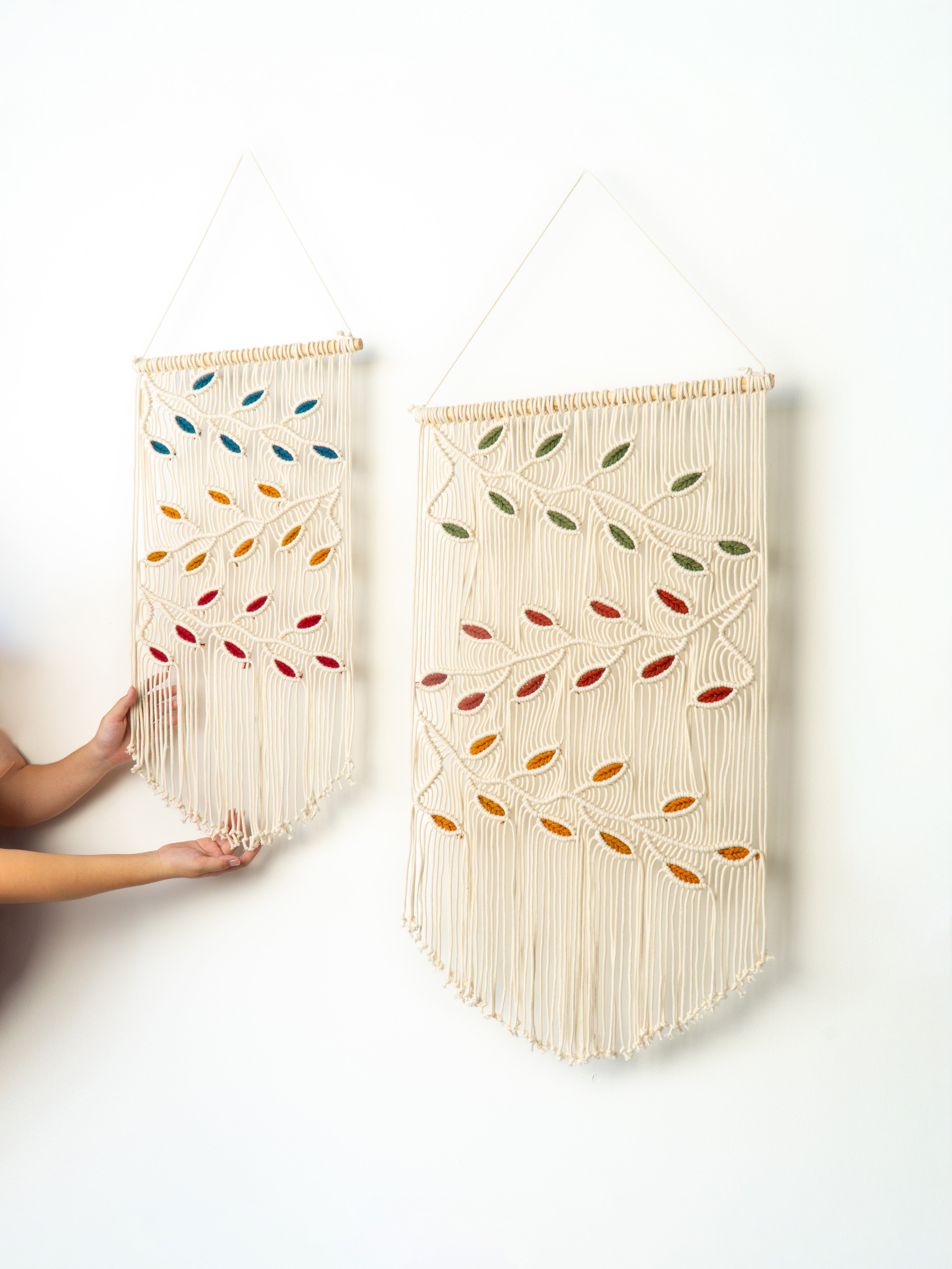 Two wall hangings with colorful leaf patterns on a white background