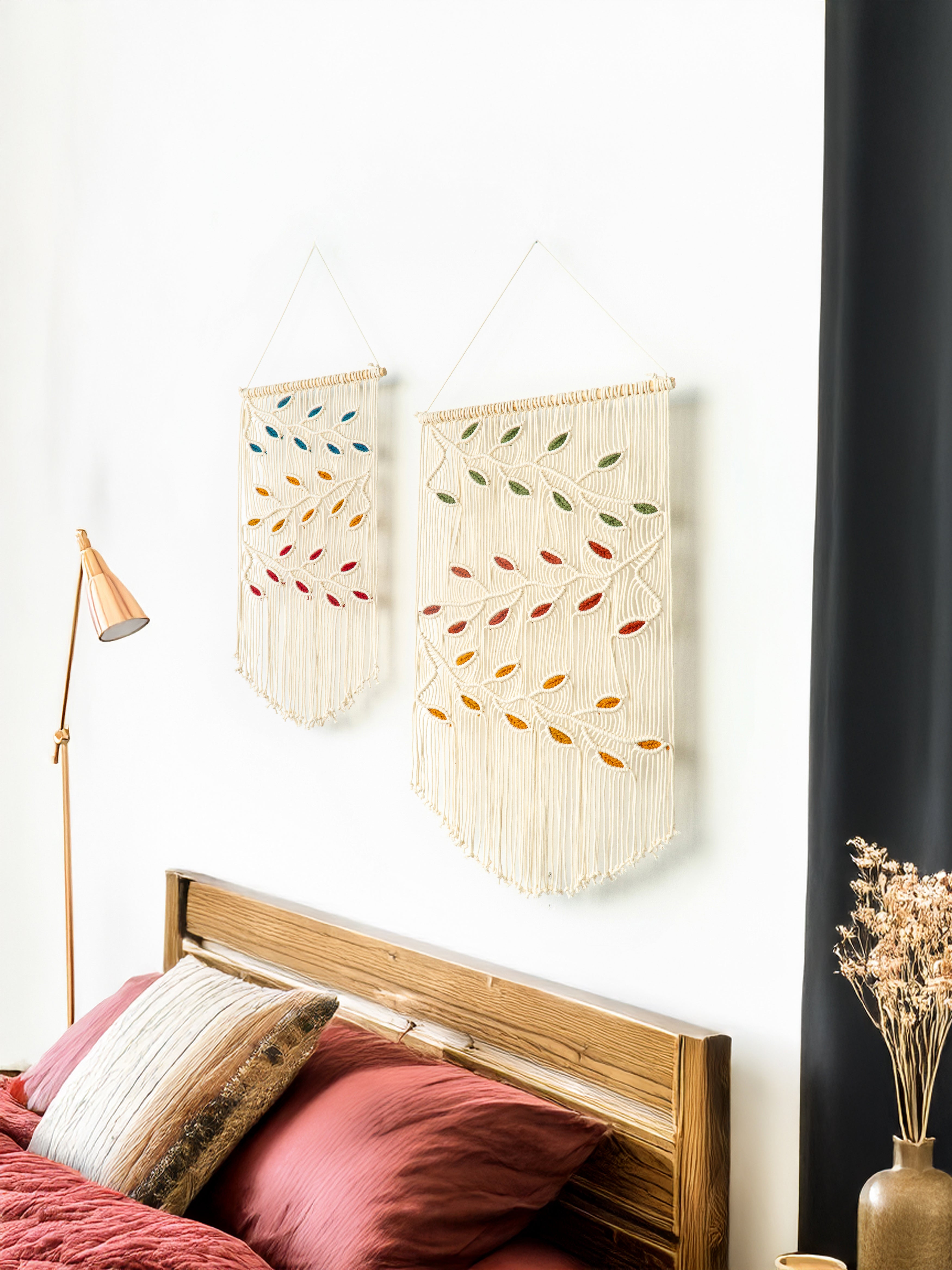 Two wall hangings with leaf patterns on a white wall above a bed with pillows.