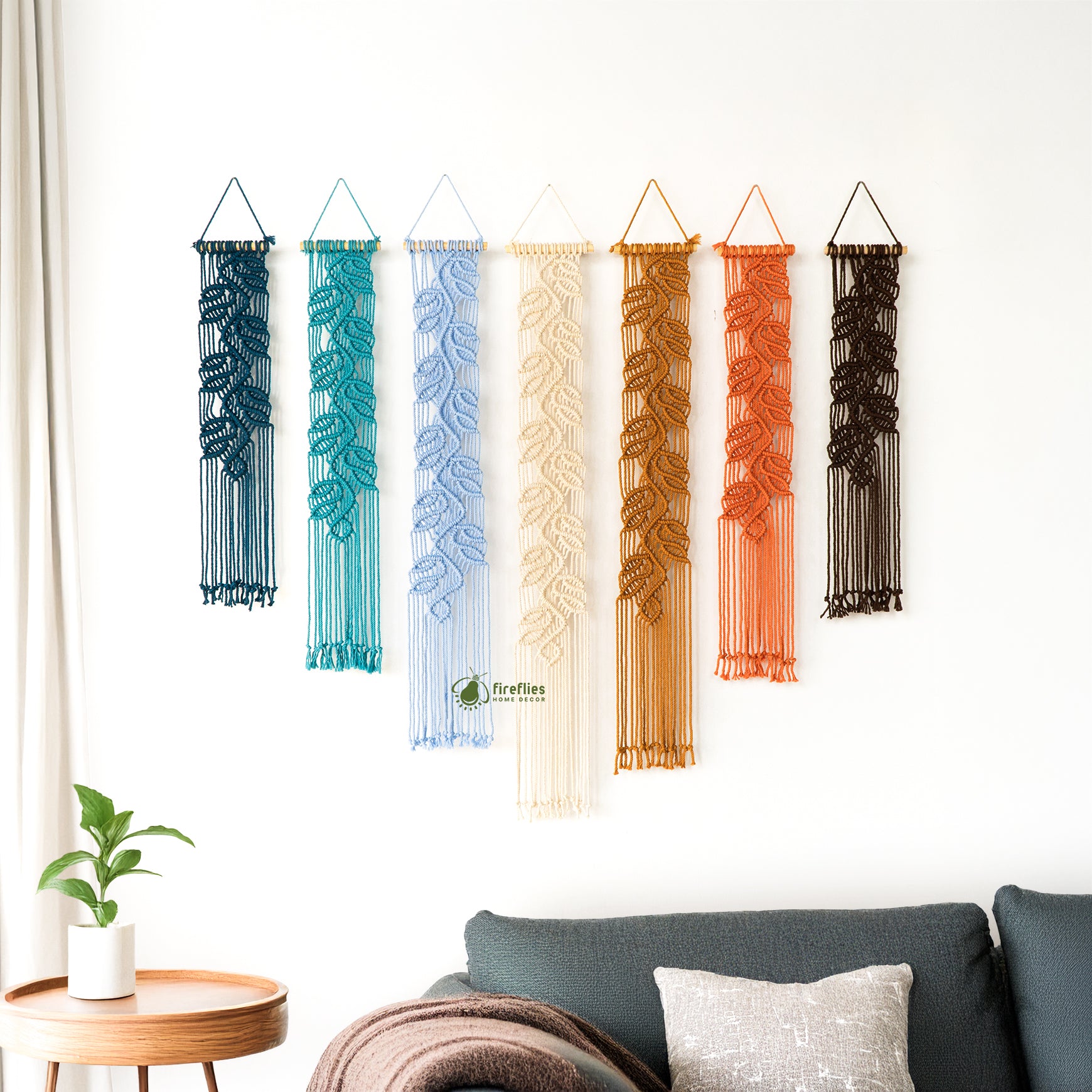Set of four macrame wall hangings with leaf patterns on a white wall above a beige sofa.