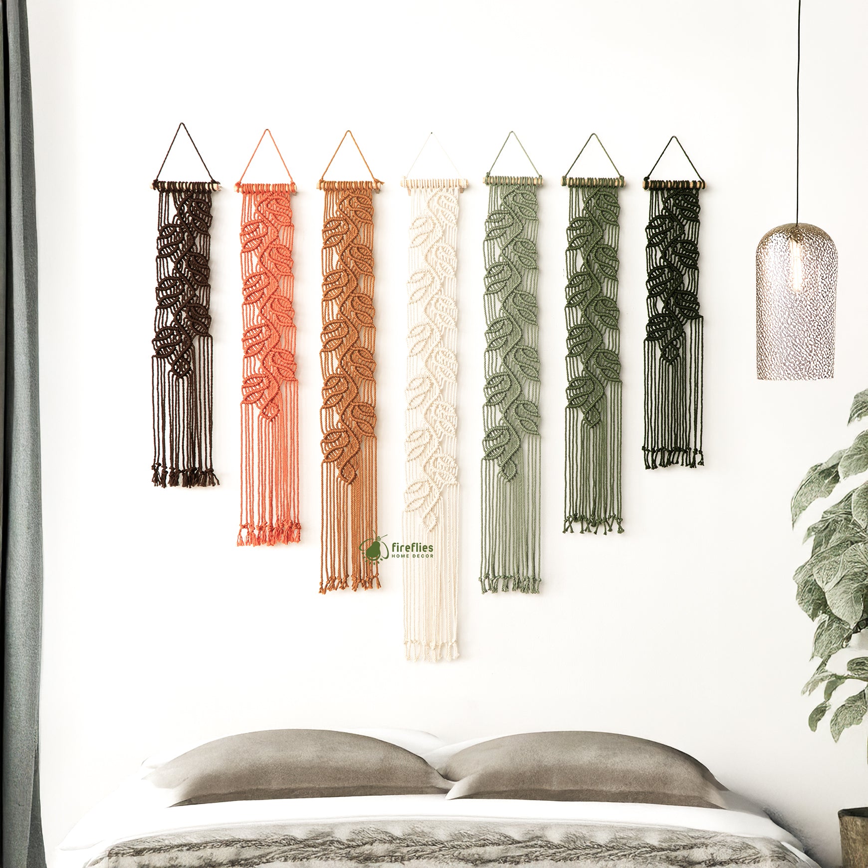 Set of six colorful wall hangings with leaf patterns on a white wall above a bed.