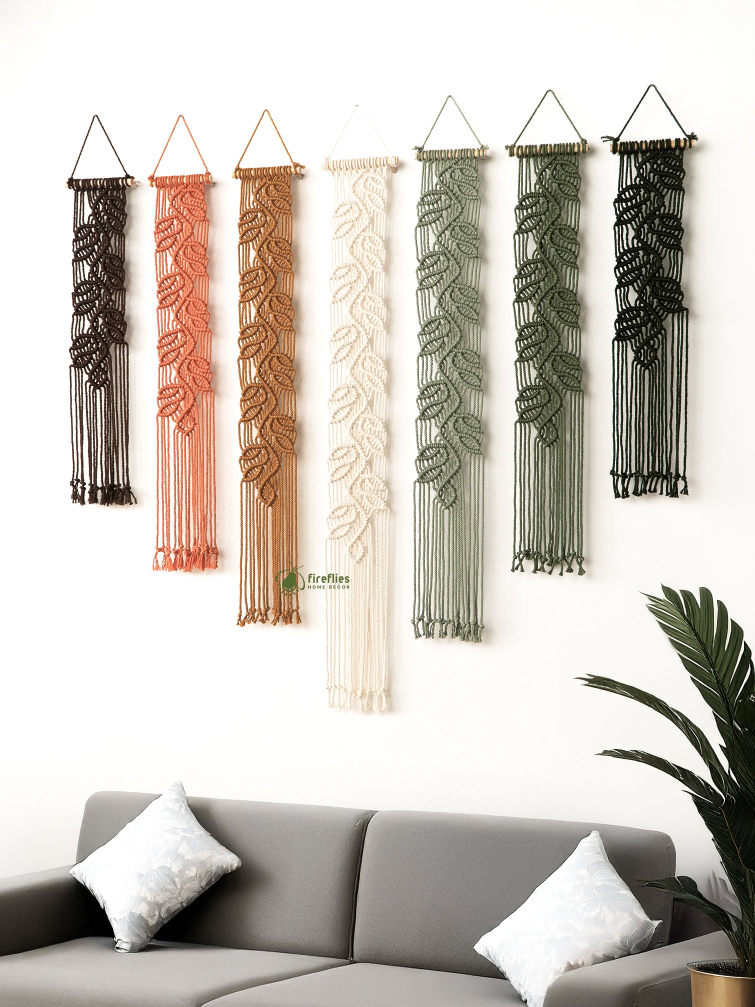 Set of six macrame wall hangings in various colors hanging above a gray sofa.