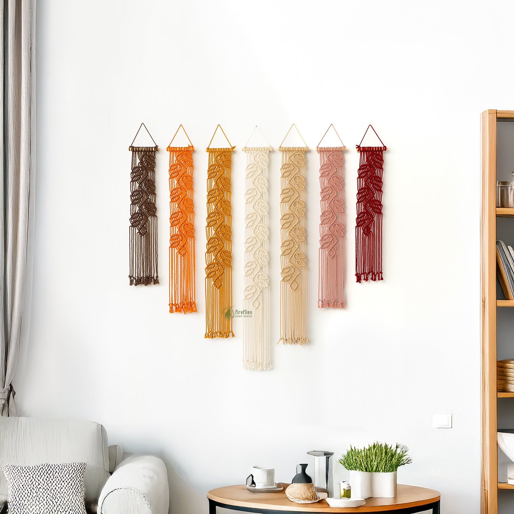Set of six macrame wall hangings in various colors hanging on a white wall.