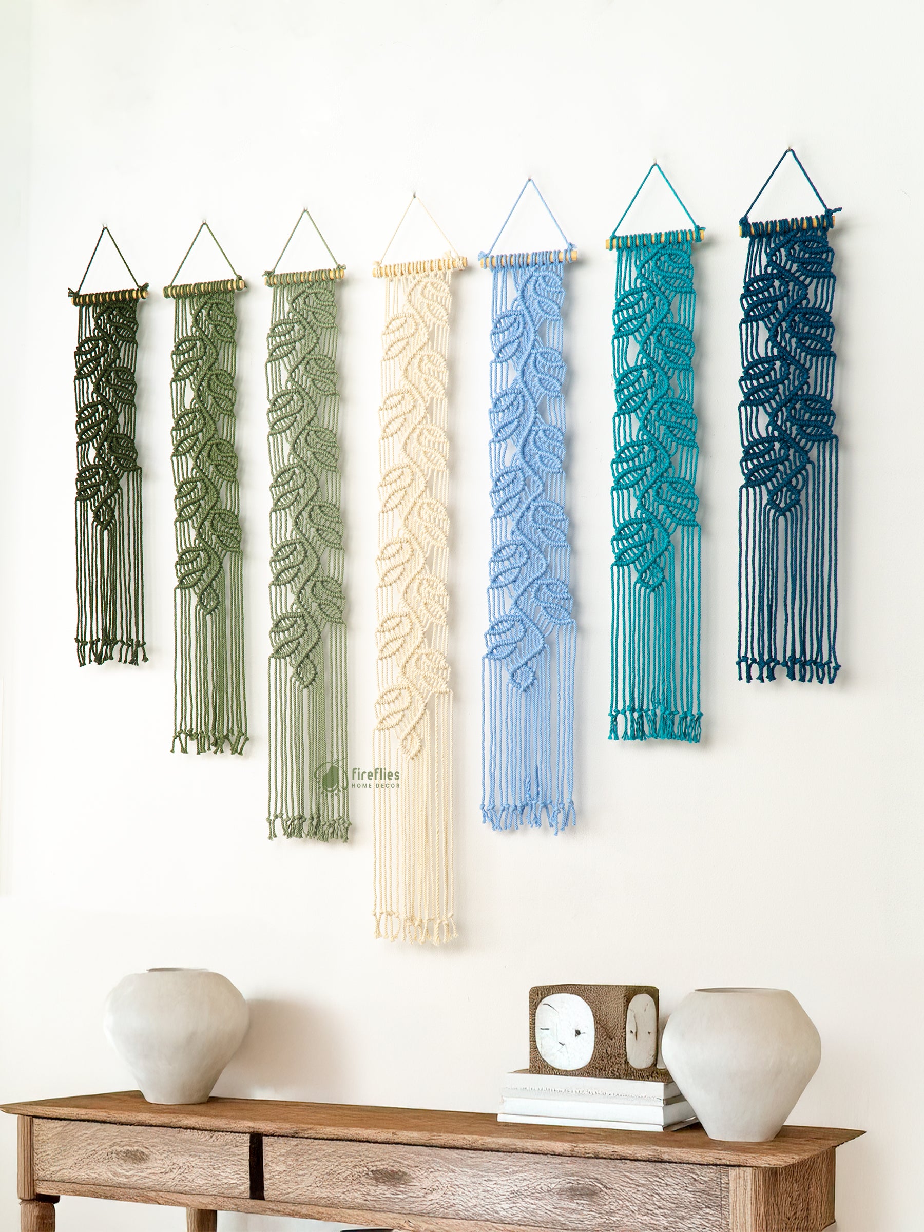 Set of six woven wall hangings in various colors hanging on a white wall above a wooden console table.