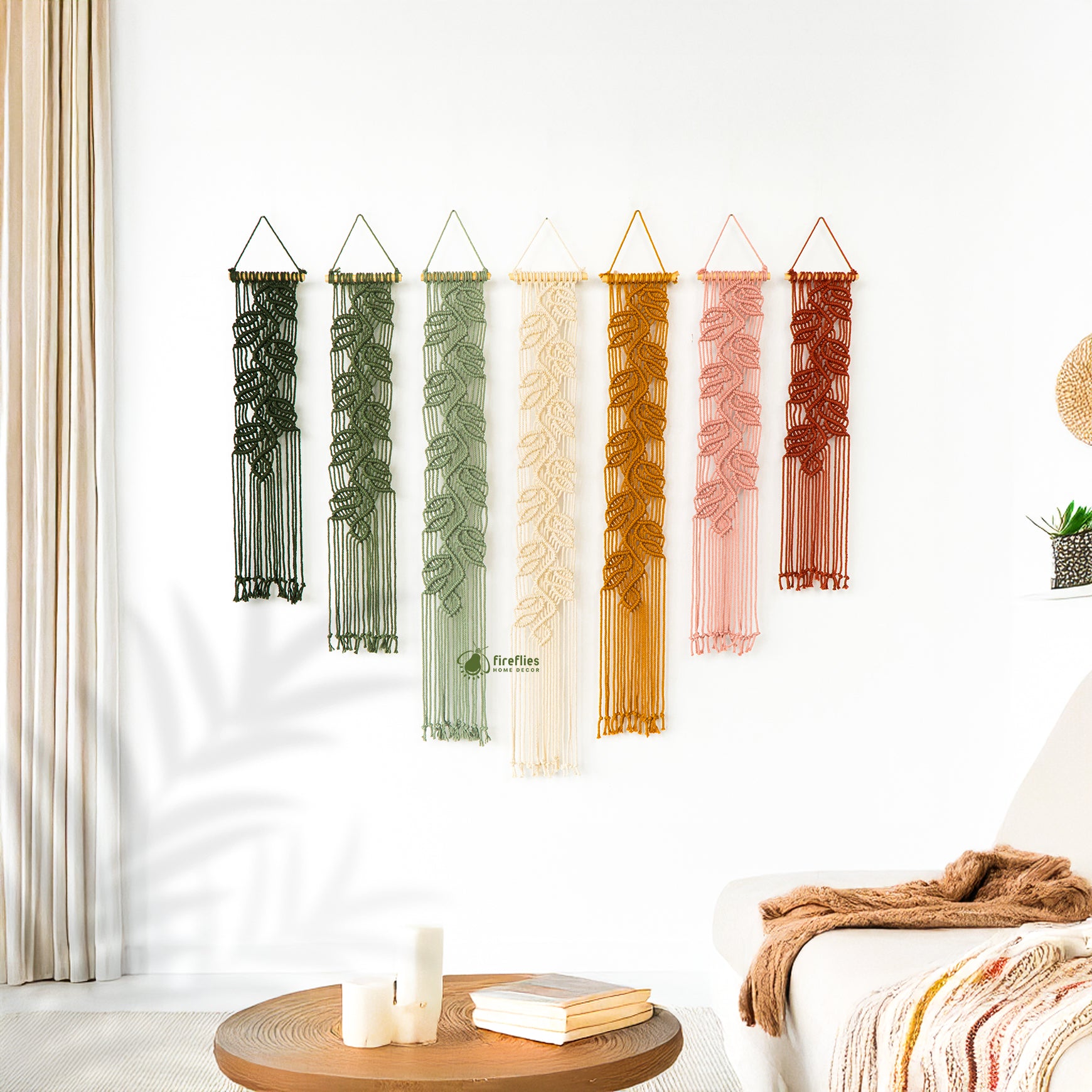 Set of colorful macrame wall hangings on a white wall with a small table and decor items below.