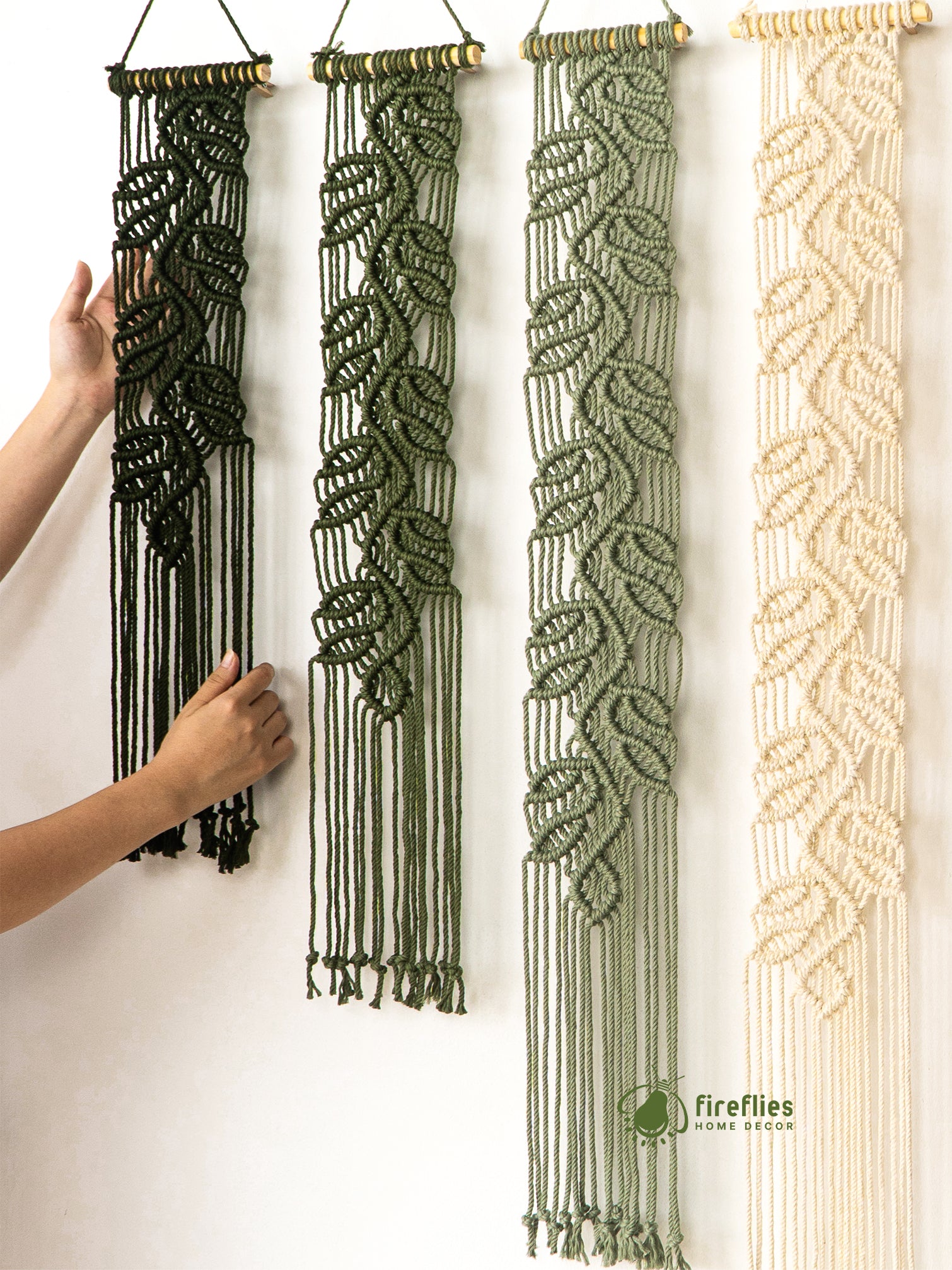 Four macrame wall hangings in different colors hanging on a white wall.