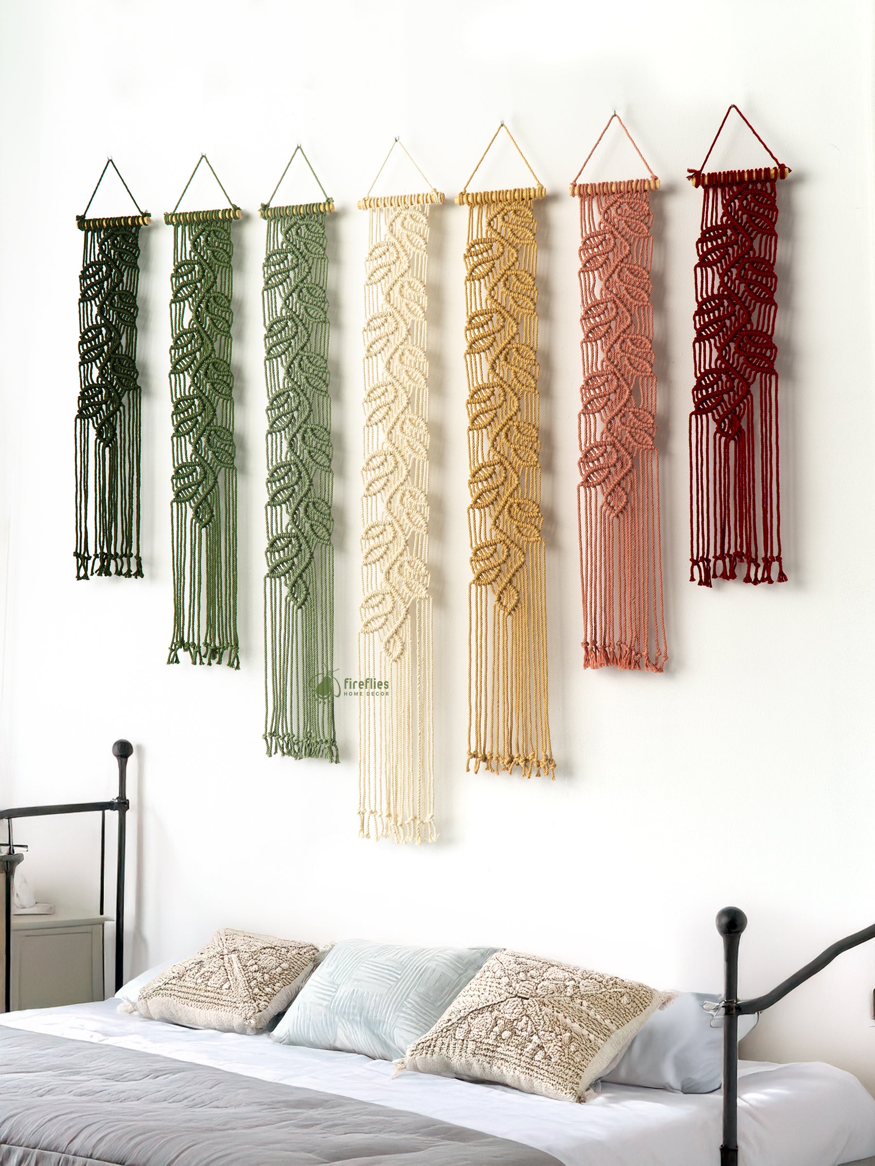 Set of six macrame wall hangings in various colors hanging above a bed.