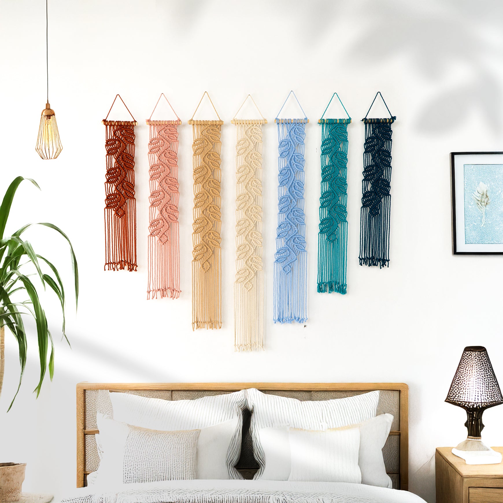 Set of colorful macrame wall hangings on a white wall above a dark green sofa.