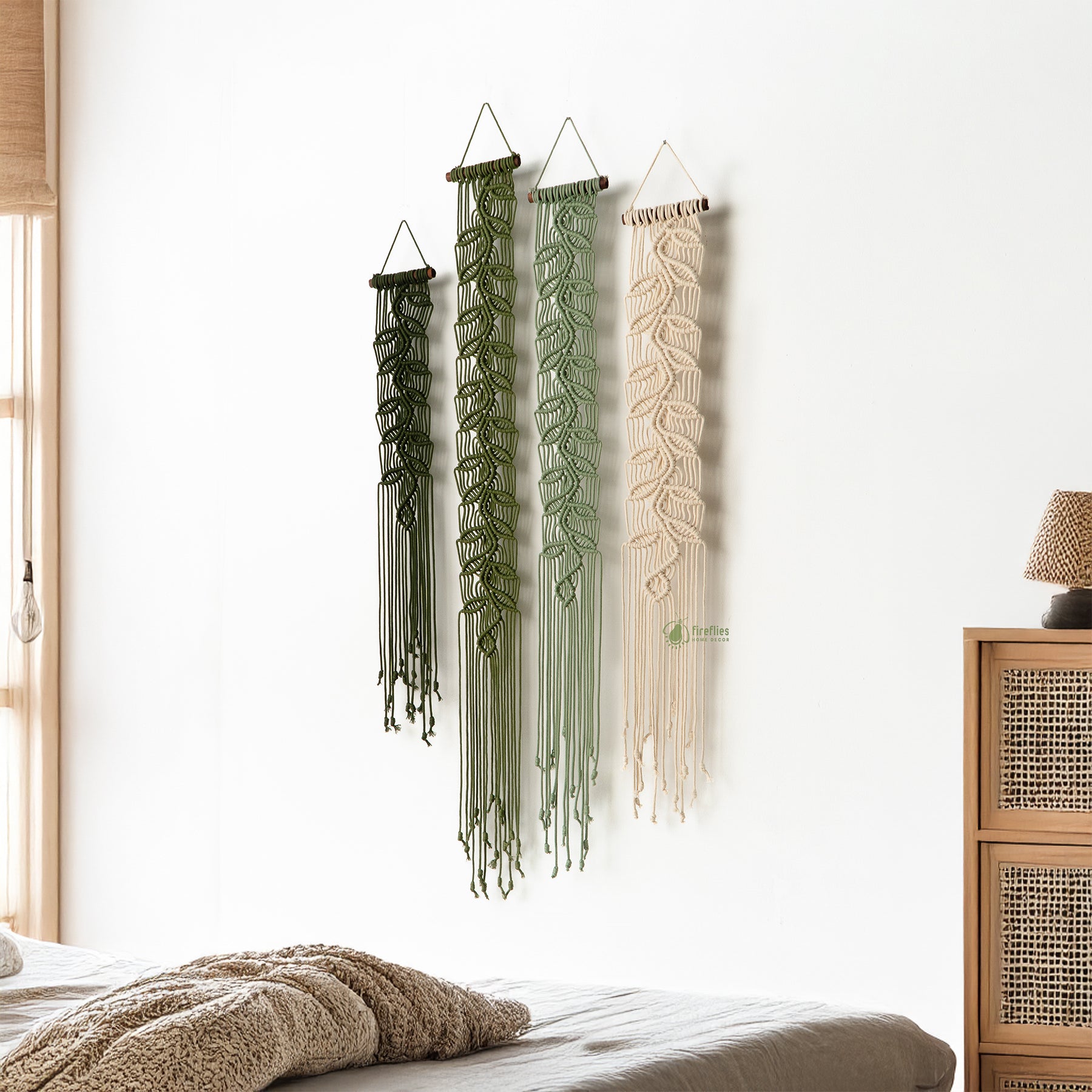 Three macrame wall hangings in different colors hanging on a white wall.