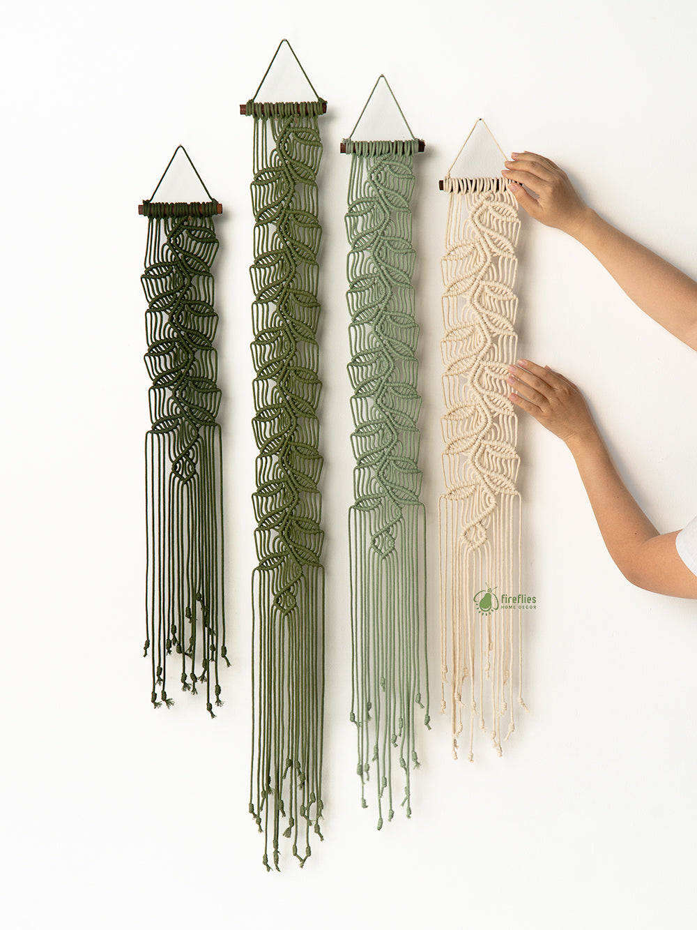 Red macramé wall hanging on a white wall with a wicker chair and wooden cabinet in the foreground.