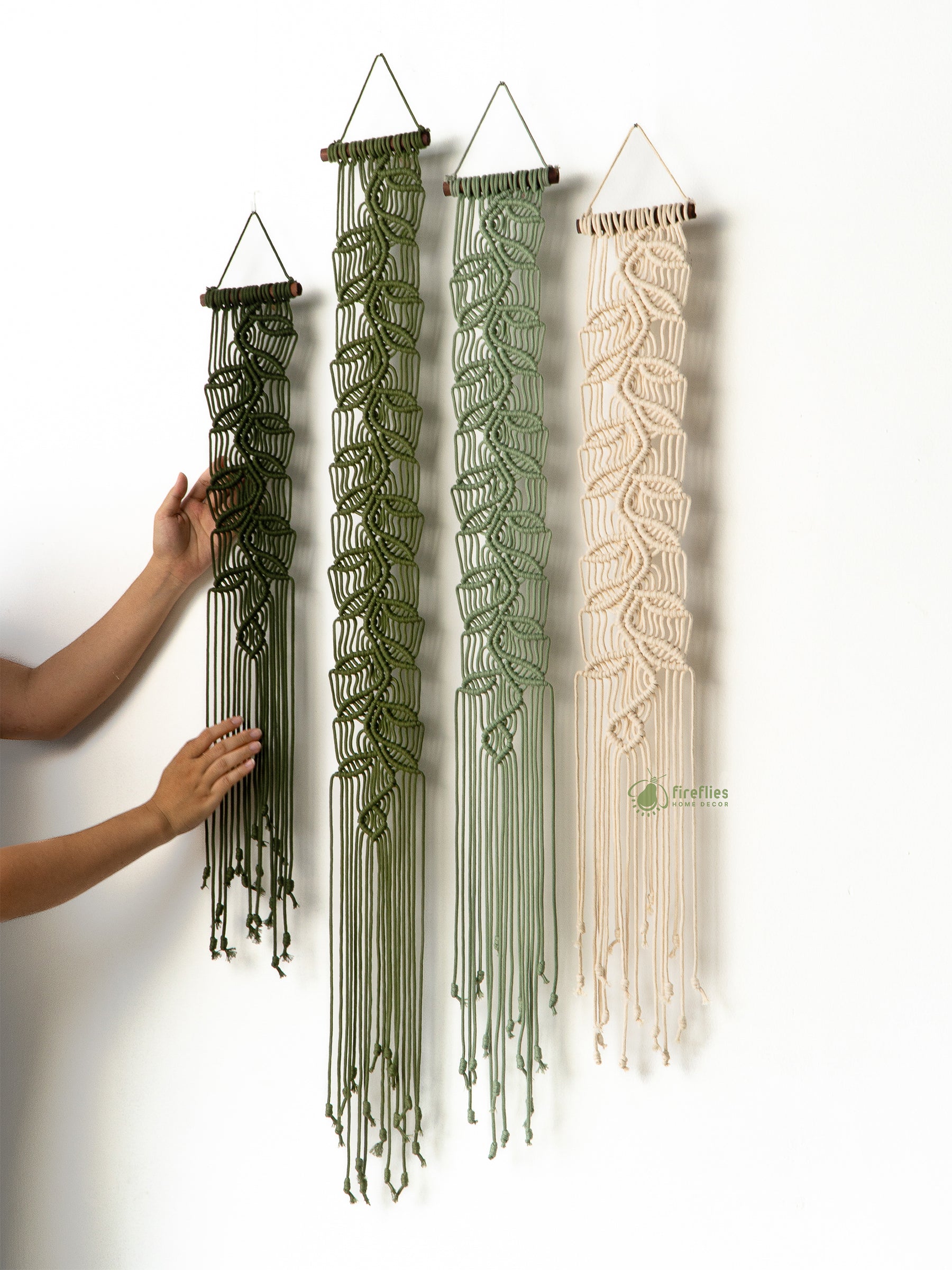 Three macrame wall hangings in green and beige hanging on a white wall.